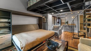 A modern bedroom with a large bed, a desk, and a chair. There is a staircase leading to an upper level. - Rc5b0 (Breckenridge)