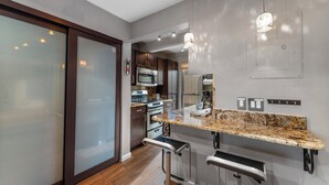 A modern kitchen with a granite countertop, stainless steel appliances, and a bar stool. - Rc5b0 (Breckenridge)