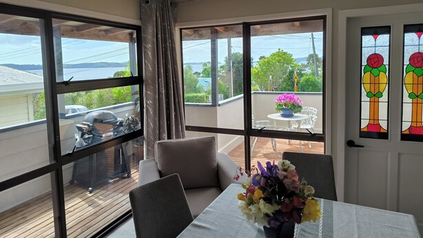 Ein Zimmer mit Balkon, großen Fenstern, einem Tisch mit Blumenvase und Blick aufs Meer.