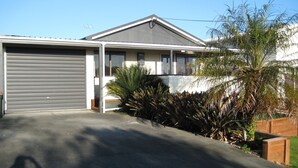 Ein modernes, zweistöckiges Haus mit Garage, überdachter Auffahrt und einem gepflegten Garten mit verschiedenen Pflanzen.