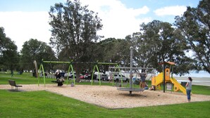 Ein Spielplatz mit Schaukeln, einer Rutsche und einer Kletterkonstruktion.