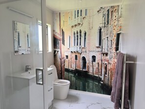 Un baño con un mural grande de un canal veneciano, un inodoro blanco, un lavabo y un perchero para toallas.