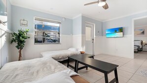 A room with two beds, a table, a ceiling fan, a window with a view, a TV, and a plant. - Boutique Beach Escape with Dock + Pool + Sunset Views (Treasure Island)
