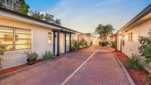 A paved walkway flanked by buildings with large windows and outdoor plants. - Boutique Beach Escape with Dock + Pool + Sunset Views (Treasure Island)
