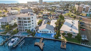 An aerial view of a coastal property with a swimming pool, docked boats, and a marina. - Boutique Beach Escape with Dock + Pool + Sunset Views (Treasure Island)