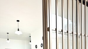 Habitación de hotel moderna con cama, escritorio y silla. Se aprecia un ventanal grande con persianas verticales y una planta en maceta sobre el alféizar.