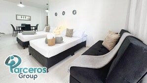 Una habitación moderna y luminosa con dos camas, un sofá, un comedor y una pequeña mesa.