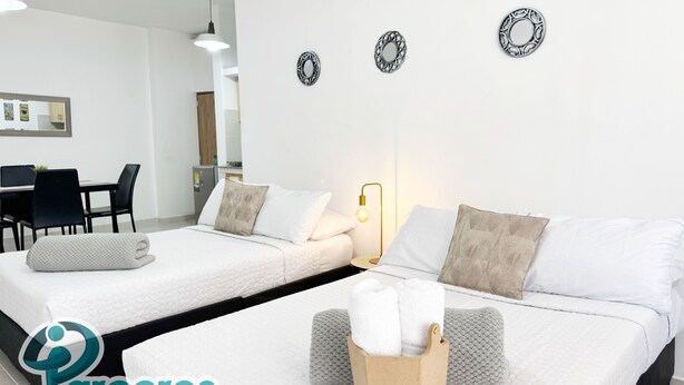 Habitación de hotel con dos camas, un escritorio y una silla. Se observan placas decorativas en la pared y una mesita con una lámpara.