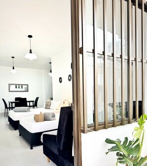 A modern hotel room with a bed, a desk, and a chair. There is a large window with vertical blinds, and a potted plant on the windowsill.
