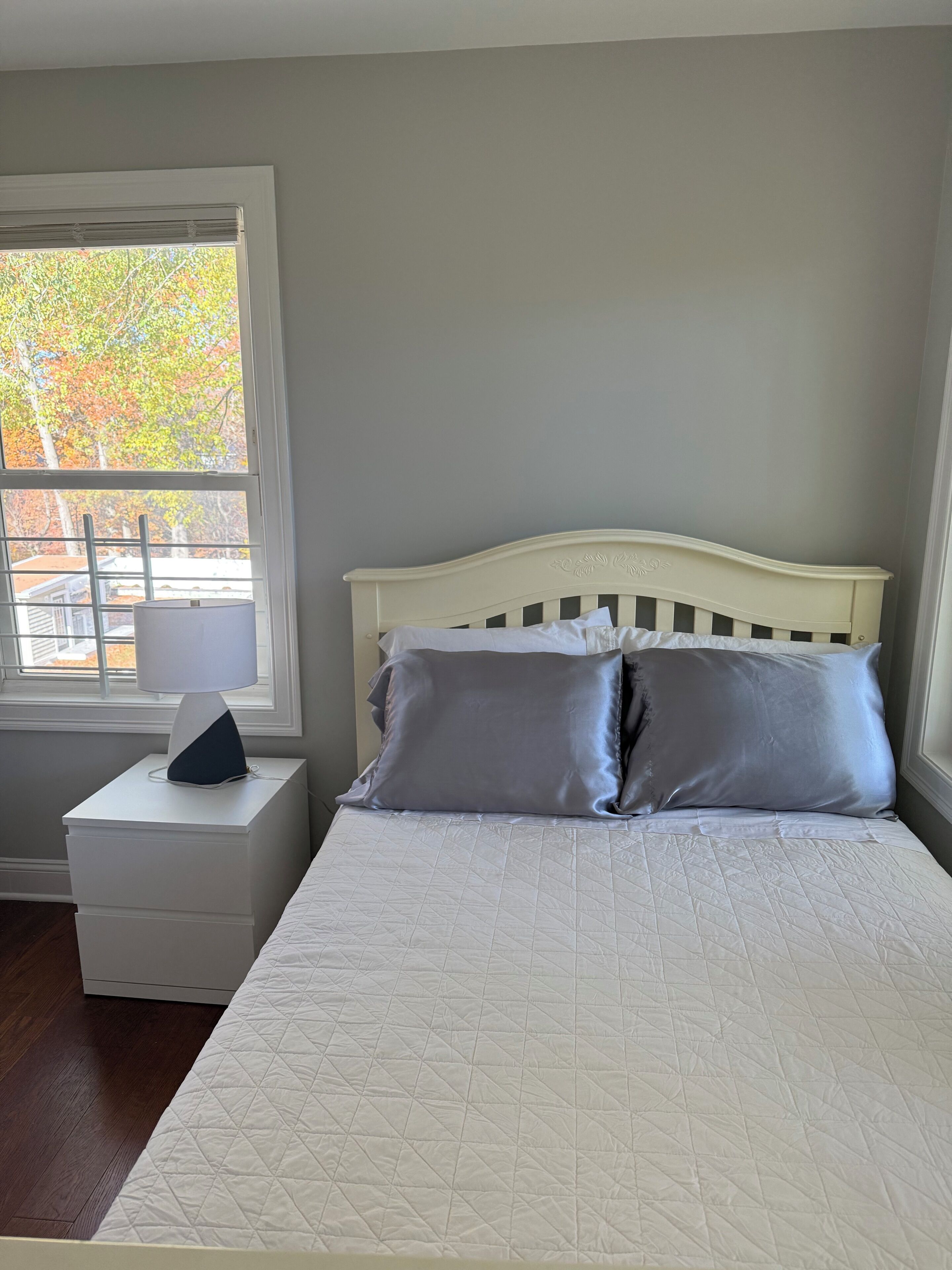 Una camera da letto con un letto, un comodino, una lampada e una finestra vista alberi.