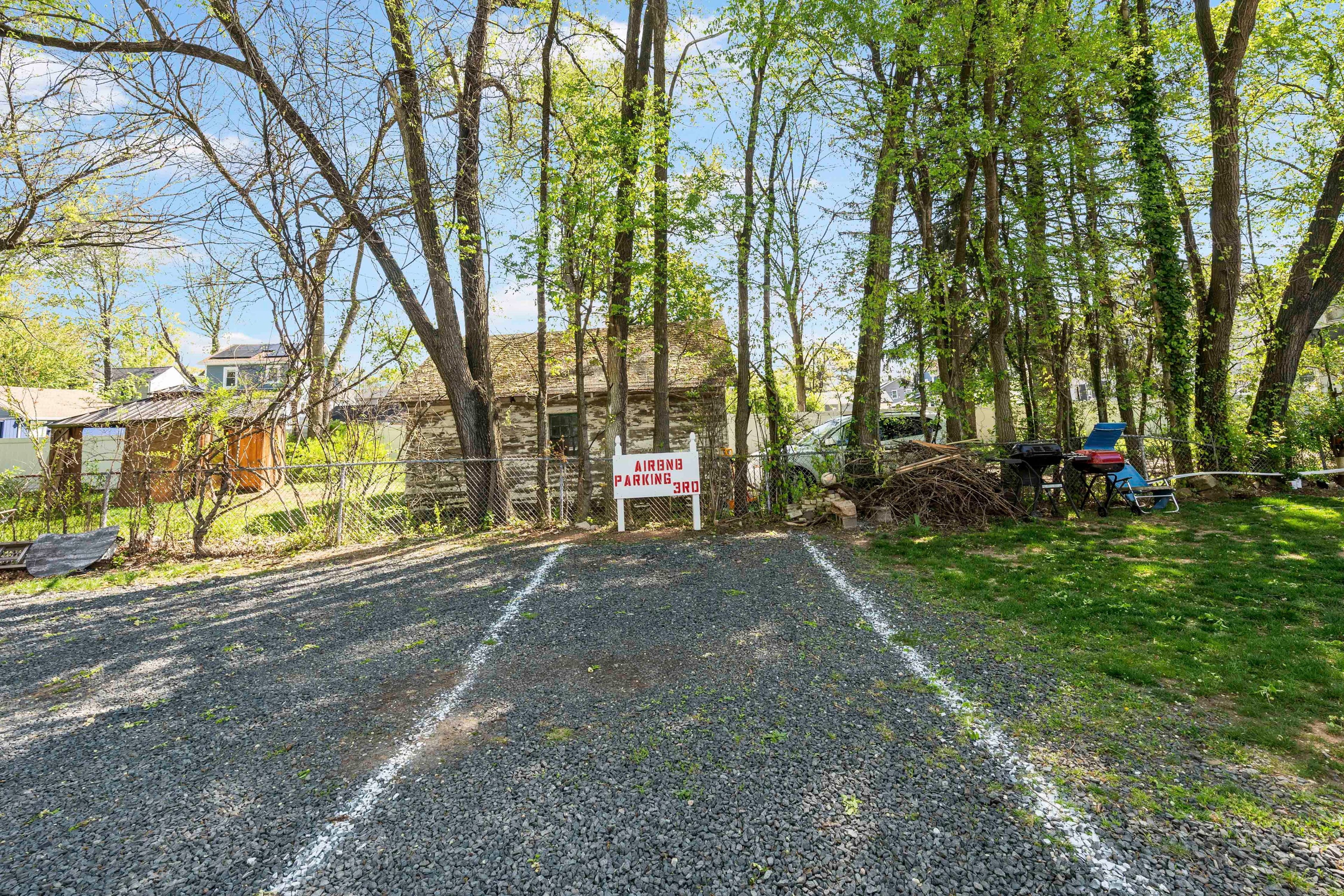Ein Schotterweg führt zu einer Holzhütte, an der ein Schild 'Airbnb Parkplatz' steht.