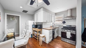 Una cocina moderna con armarios blancos, horno empotrado y un comedor con mesa de vidrio y sillas blancas.