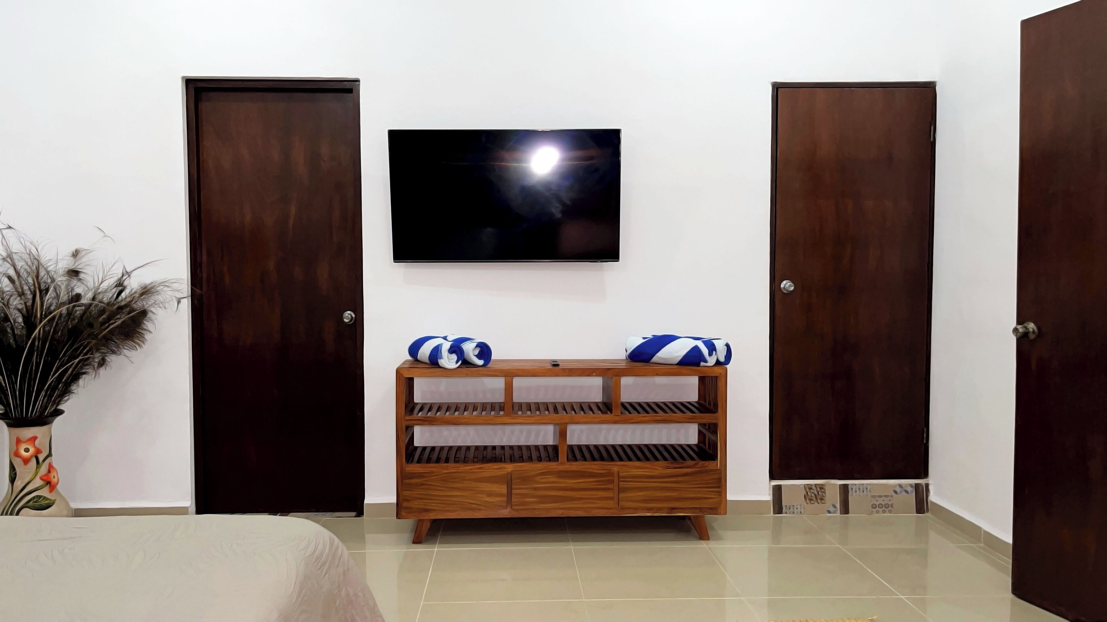 A hotel room with a bed, a wooden bench with pillows, a television, and two doors.