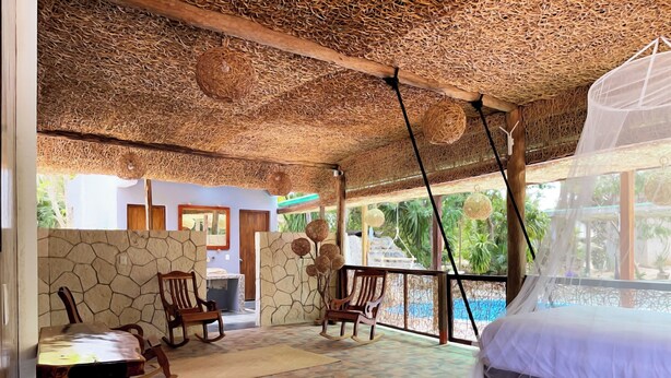 Una habitación con techo de paja, paredes de piedra y una cama con mosquitero.