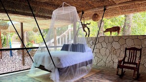 Una habitación con una cama bajo una mosquitera, pared de piedra y una silla de madera.