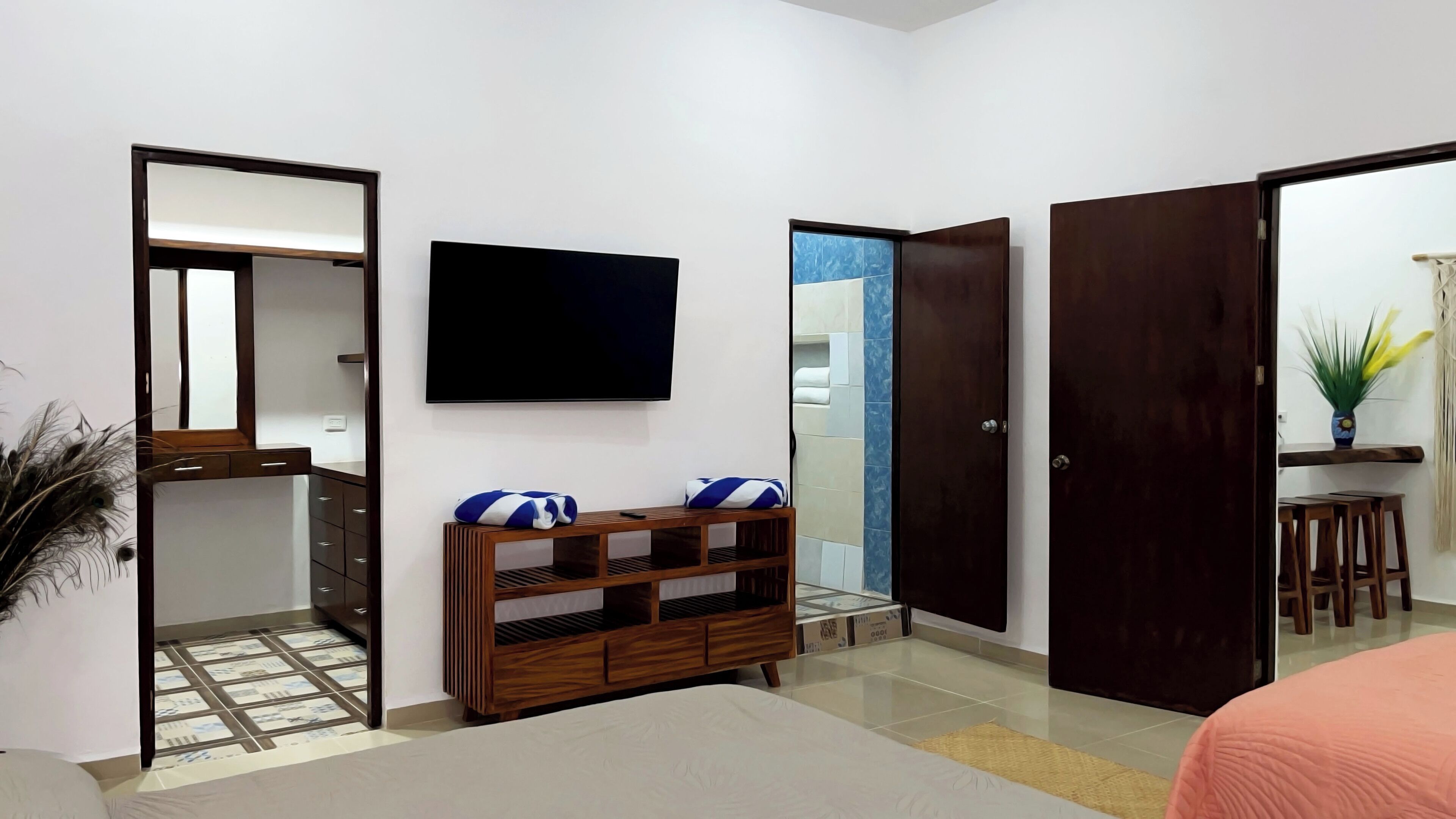 Un dormitorio con cama, televisor, armario y baño a la vista a través de una puerta abierta.