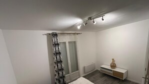 A bedroom with a bed, a nightstand, a bedside table, a radiator, and a window with curtains. - Apartment le Bugatti 4 persons wifi (Yvré-l'Évêque)