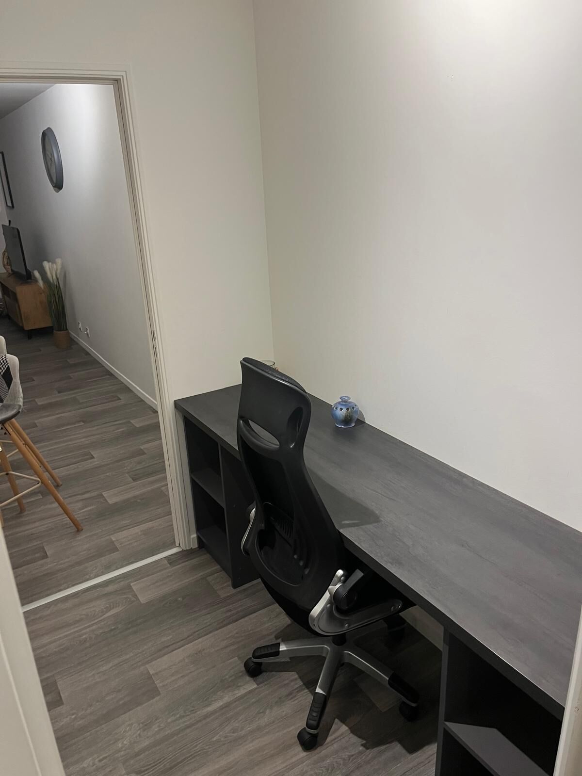 Een moderne kantoorruimte met een lang bureau, een zwarte bureaustoel en een klein decoratief object op het bureau.