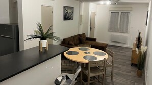 A modern living space with a round dining table, a sofa, a refrigerator, and a potted plant. - Apartment le Bugatti 4 persons wifi (Yvré-l'Évêque)