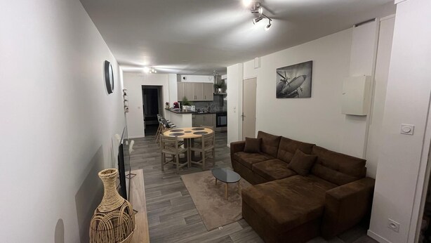 A modern living space with a brown sofa, a dining table with chairs, and a kitchen in the background. - Apartment le Bugatti 4 persons wifi (Yvré-l'Évêque)