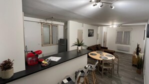 A modern kitchen with a black countertop, a red kettle, and a small plant. There is a dining area with a round table and four chairs. - Apartment le Bugatti 4 persons wifi (Yvré-l'Évêque)