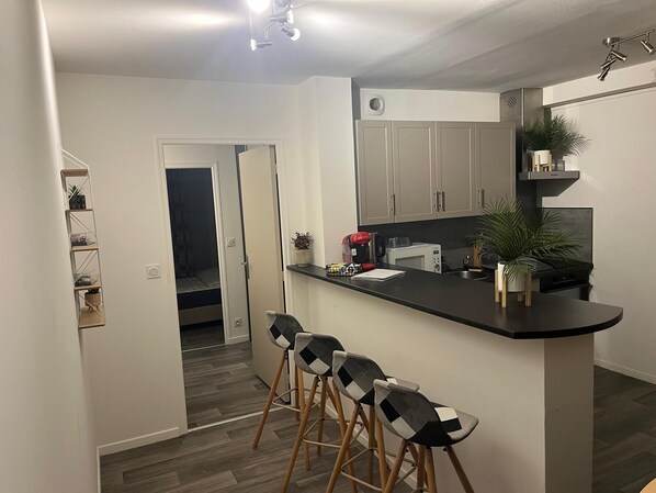 A modern kitchen with a black countertop, stainless steel appliances, and a seating area with bar stools.