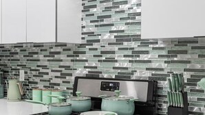 Een moderne keuken met een gasfornuis, oven en vaatwasser. Op het aanrecht staan groene pannen en een messenblok.