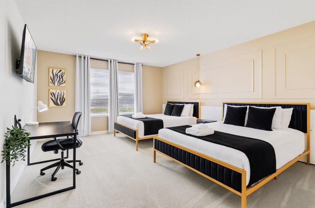 A hotel room with two beds, a desk, a chair, and a TV.
