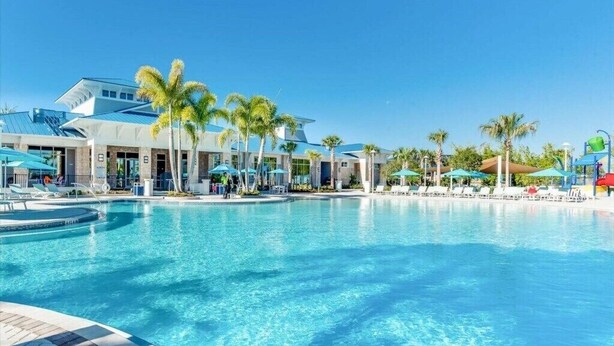 Ein Swimmingpool mit Liegestühlen und Palmen, umgeben von einem Gebäude mit blauem Dach.