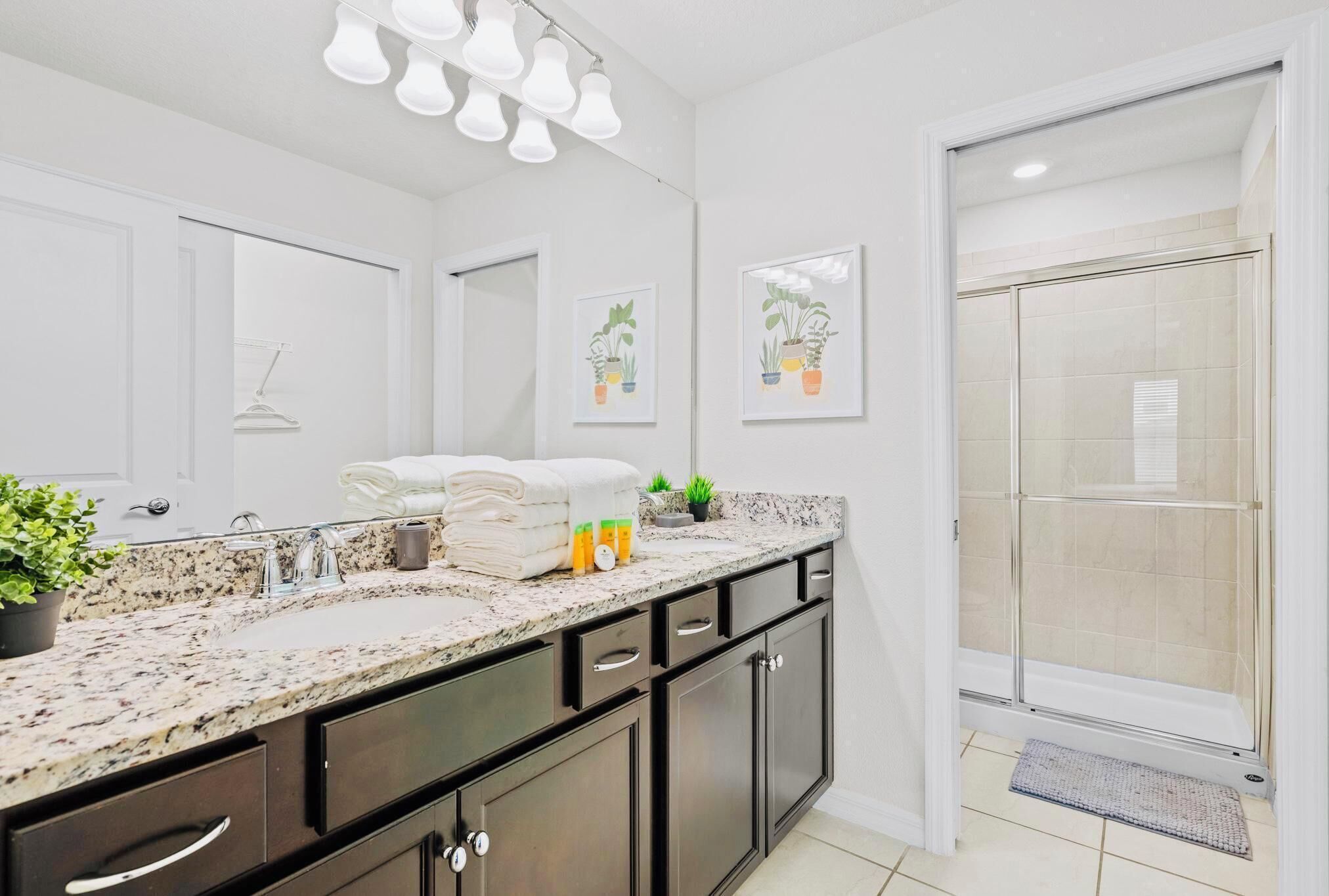 A modern bathroom with a granite countertop, dark cabinetry, a large mirror, and a shower area with a glass door.