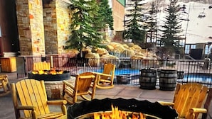 A patio area with wooden chairs, a fire pit, and a poolside view of a mountain landscape.