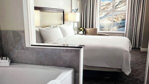 A hotel room with a bed, a chair, a window with curtains, and a view of a mountainous landscape.
