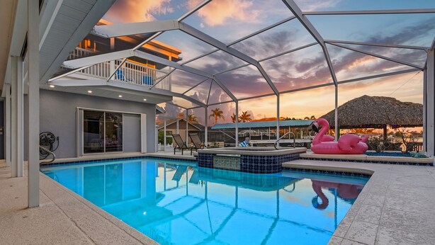 A swimming pool with a glass ceiling, a pink flamingo float, and a thatched-roof structure. - 19th Place Paradise Awaits! (Cape Coral)