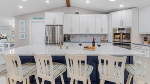 A modern kitchen with white cabinets, stainless steel appliances, and a central island with bar stools. - 19th Place Paradise Awaits! (Cape Coral)