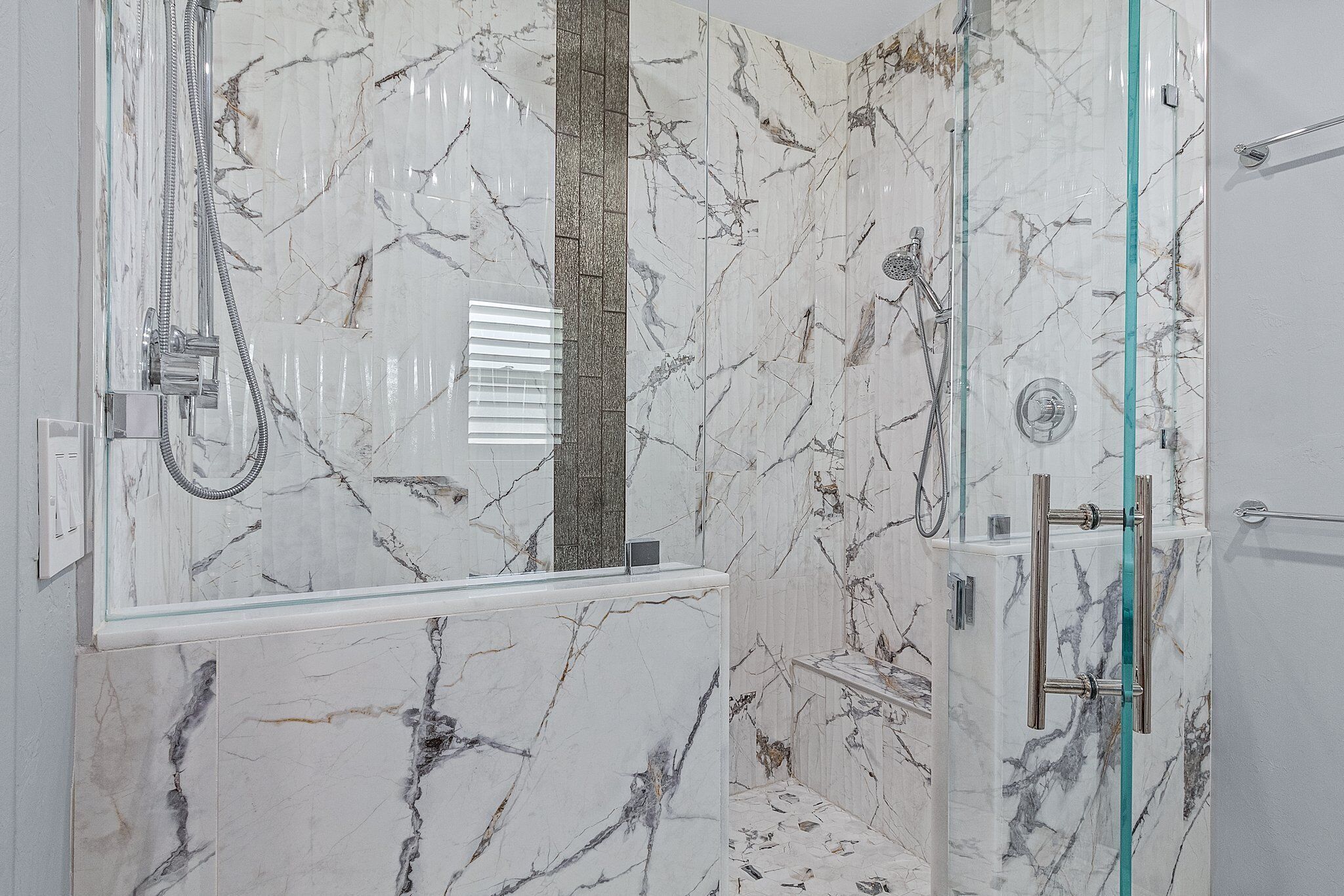 A modern bathroom with marble walls, a glass shower enclosure, and a white sink.