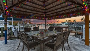 An outdoor dining area with a thatched roof, wicker furniture, and colorful hanging lights. - 19th Place Paradise Awaits! (Cape Coral)