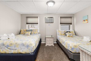 A twin room with two beds, a small table, a nightstand, and an air conditioning unit.