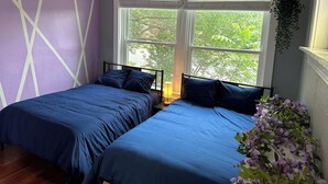 A bedroom with two beds, a large window, and a ceiling fan.