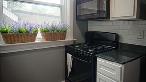 A kitchen with a stove, oven, microwave, and two wicker baskets with lavender plants on the windowsill.