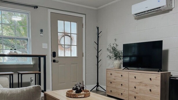 Un salon comprenant un canapé, une table basse, un téléviseur posé sur un meuble en bois et une fenêtre donnant sur des arbres.