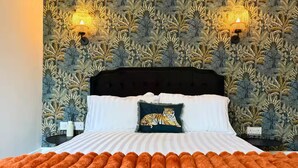 A bed with a tiger-themed pillow, a dark headboard, and a patterned wallpaper with two wall-mounted lights.