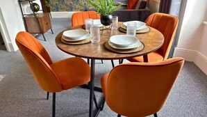 A dining area with a round wooden table, four orange chairs, and a potted plant.