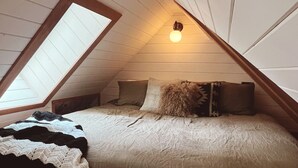 A cozy attic bedroom with a sloped ceiling, a large window, a bed with a quilt, and a single wall-mounted light. - Cozy lake-view cabin in Carnelian Bay (Carnelian Bay)