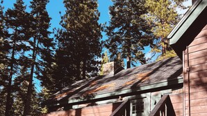 A wooden staircase with a unique railing design leading to a building with a stone chimney. - Cozy lake-view cabin in Carnelian Bay (Carnelian Bay)