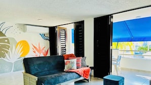 A modern living room with a dark sofa, colorful cushions, and a blue ottoman. - Your getaway space walking distance to the beach (Luquillo Luquillo)