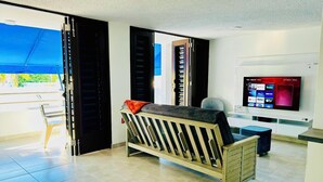 A modern living room with a sofa, a television, and a sliding door leading to a balcony. - Your getaway space walking distance to the beach (Luquillo Luquillo)