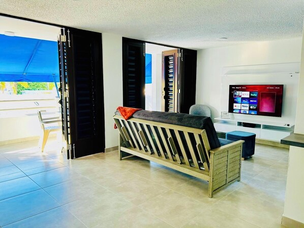 A modern living room with a sofa, a television, and a sliding door leading to a balcony.