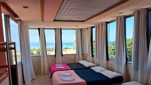 Une chambre d’hôtel avec trois lits, de grandes fenêtres et une vue sur la mer.