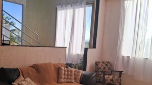 Un salon moderne avec un canapé, un fauteuil à motifs, un tapis moelleux et une télécommande posée sur un tabouret.