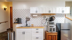Een keuken met witte kasten, een roestvrijstalen prullenbak, een houten kast, een magnetron, een broodrooster en een koelkast.
